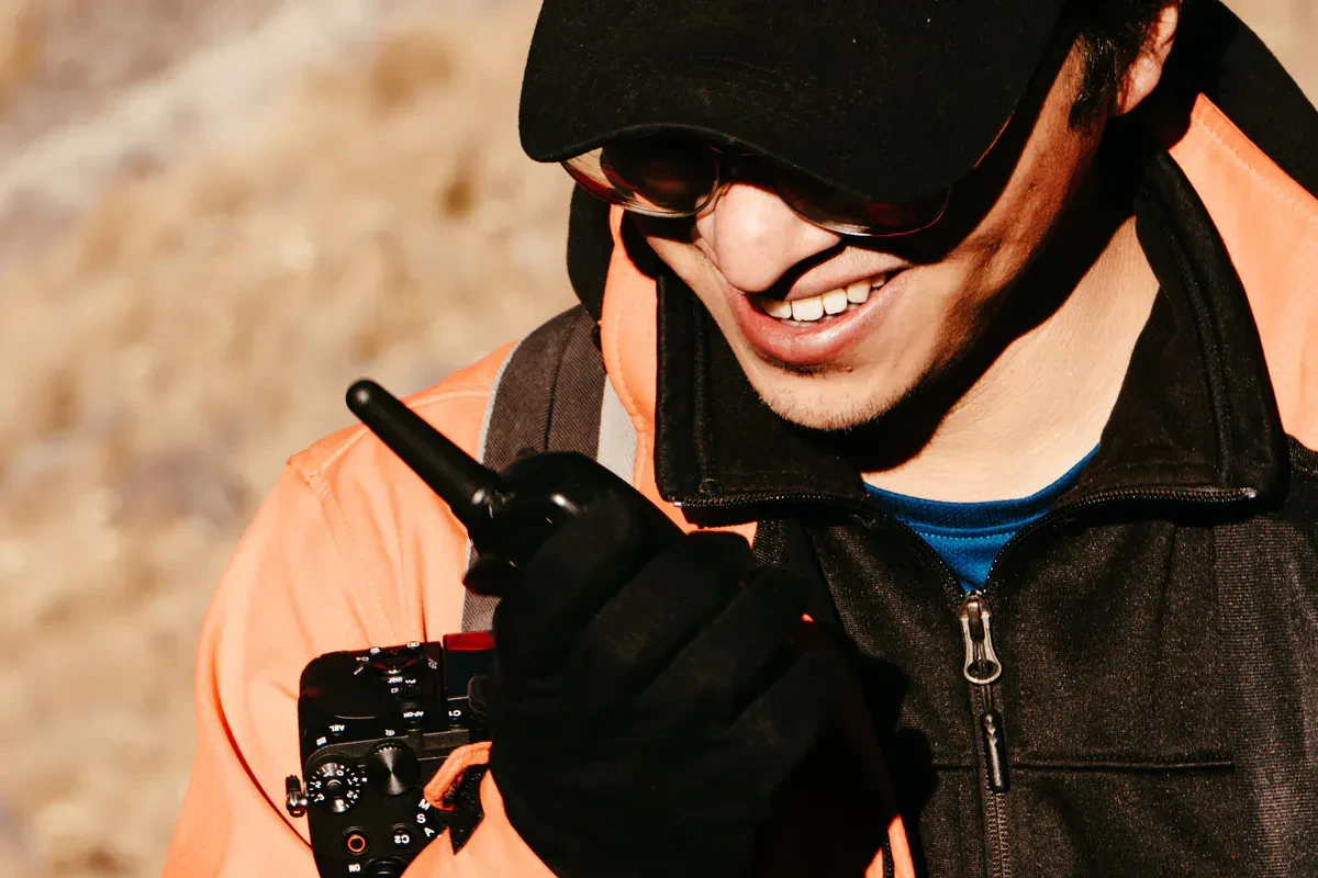 A man in an orange jacket keying up a handheld two-way radio outdoors, running an off-grid radio check where cell service drops