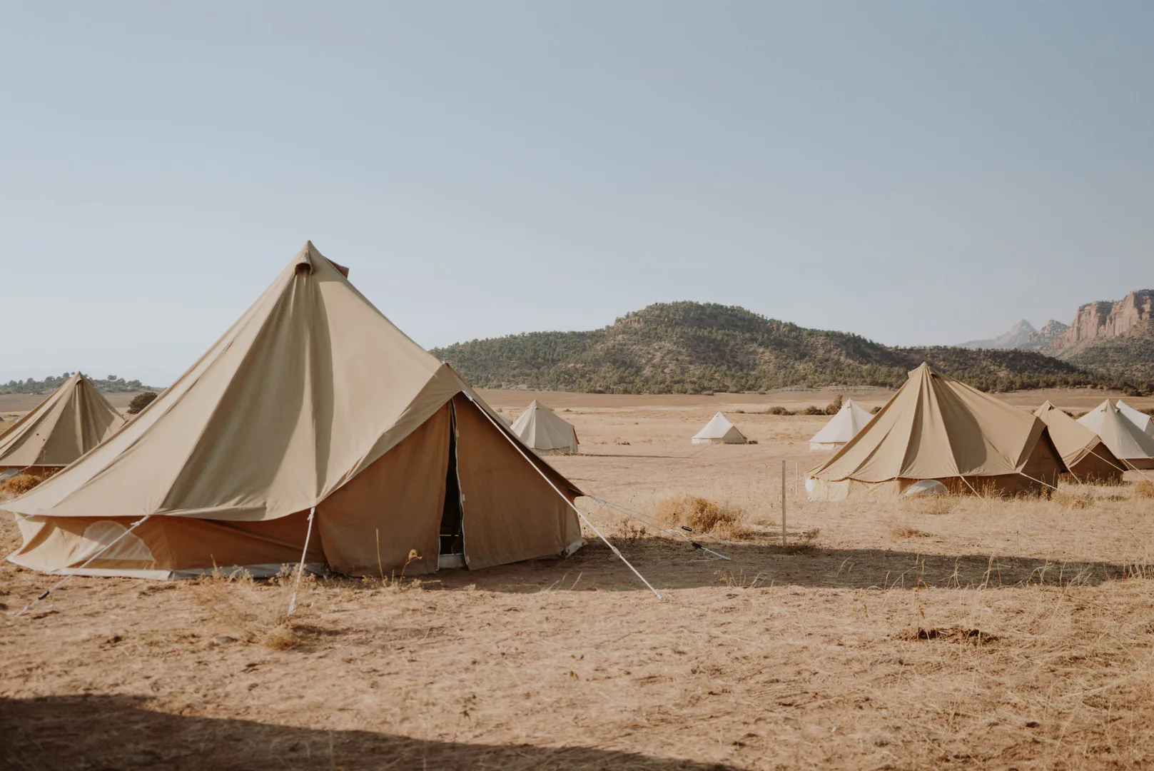 Camping tents pitched on dry sandy desert terrain near scrub-covered hills in summer heat