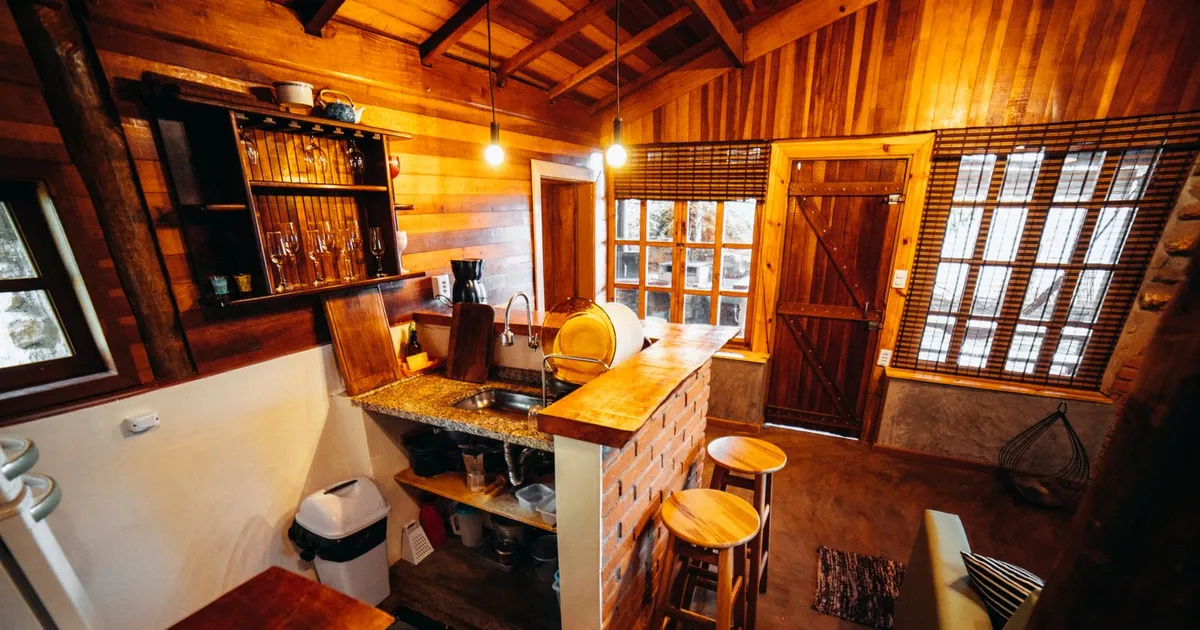 A small wood-paneled cabin kitchen with a counter and stools, the kind of space where an off-grid fridge has to fit