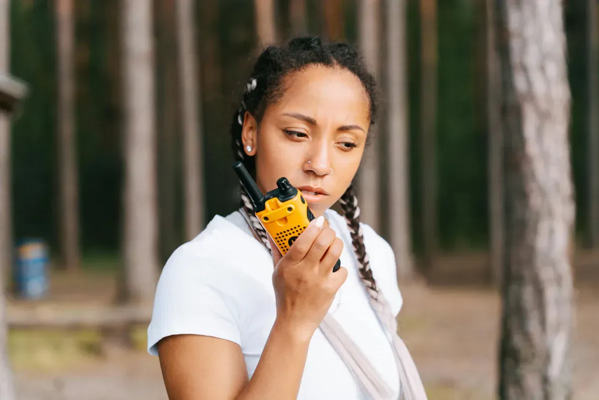 A hiker holding a handheld GMRS radio at a forest trailhead, checking in with the group during an off-grid trip