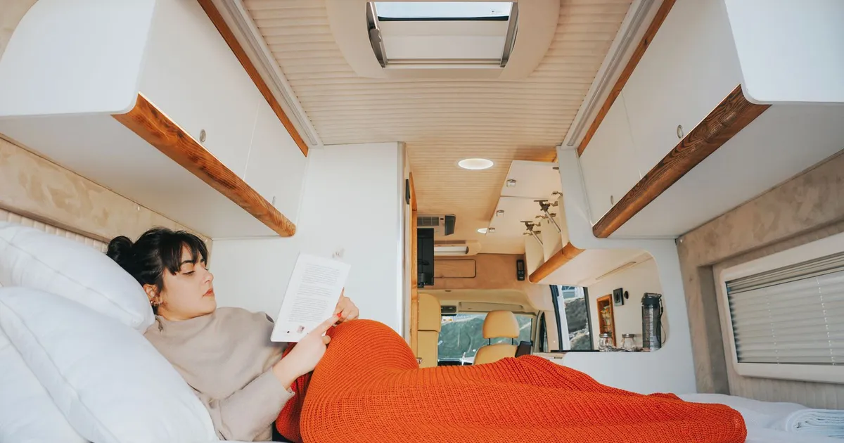 A woman reading in a camper van bed under a warm blanket on a cold morning