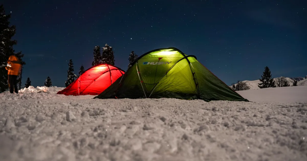 Two lit tents on snowy ground under a clear night sky, a cold-weather camp where a 12V blanket earns its place