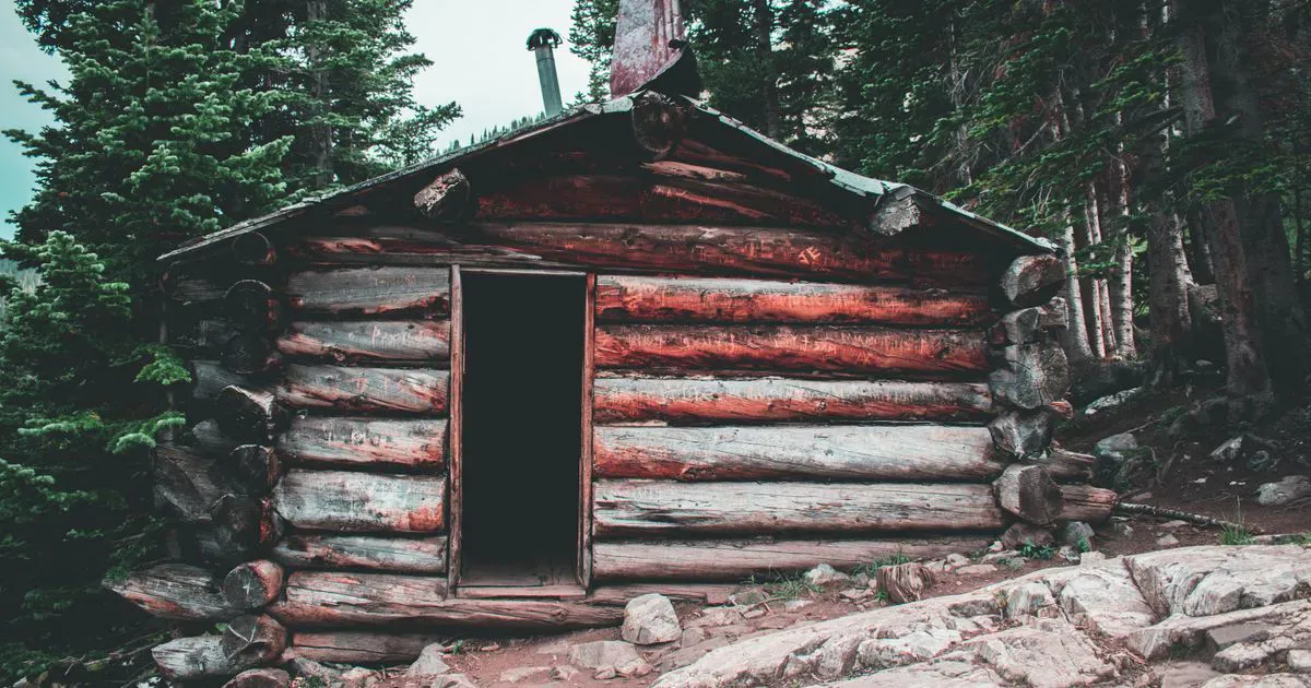 A log cabin tucked into a dense forest clearing, the kind of remote off-grid property a solar security camera has to watch without power or wifi