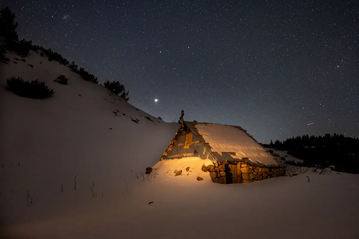 A small off-grid cabin lit up at night under a clear star-filled sky, the kind of wide-open sky view satellite internet depends on