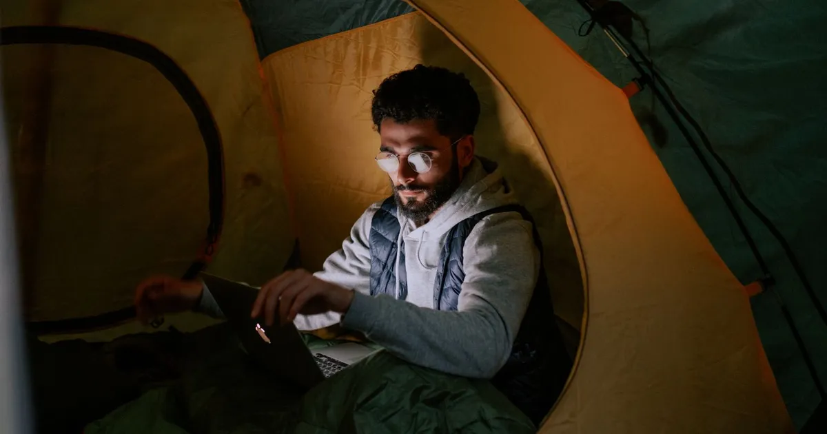 A man working on a laptop inside a tent at night