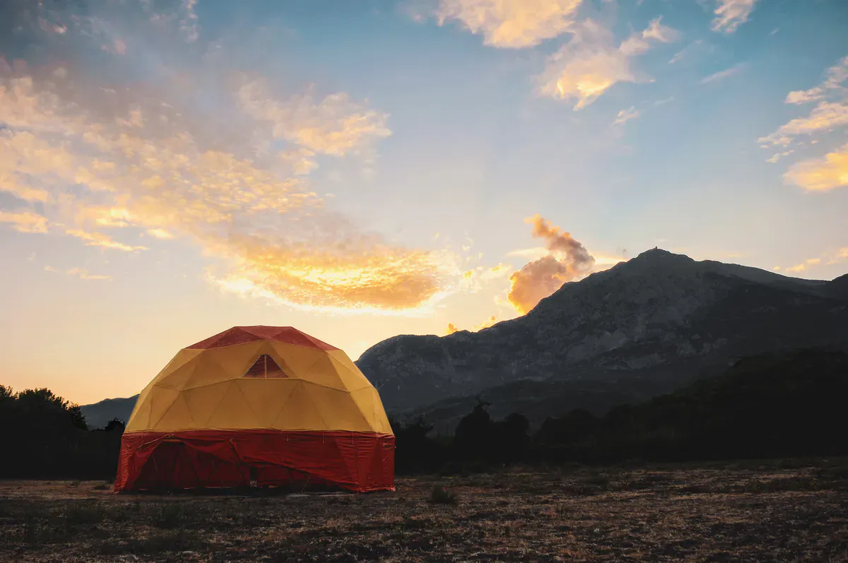 A tent pitched in open mountain country at sunset, far beyond cell coverage where satellite internet is the only way online