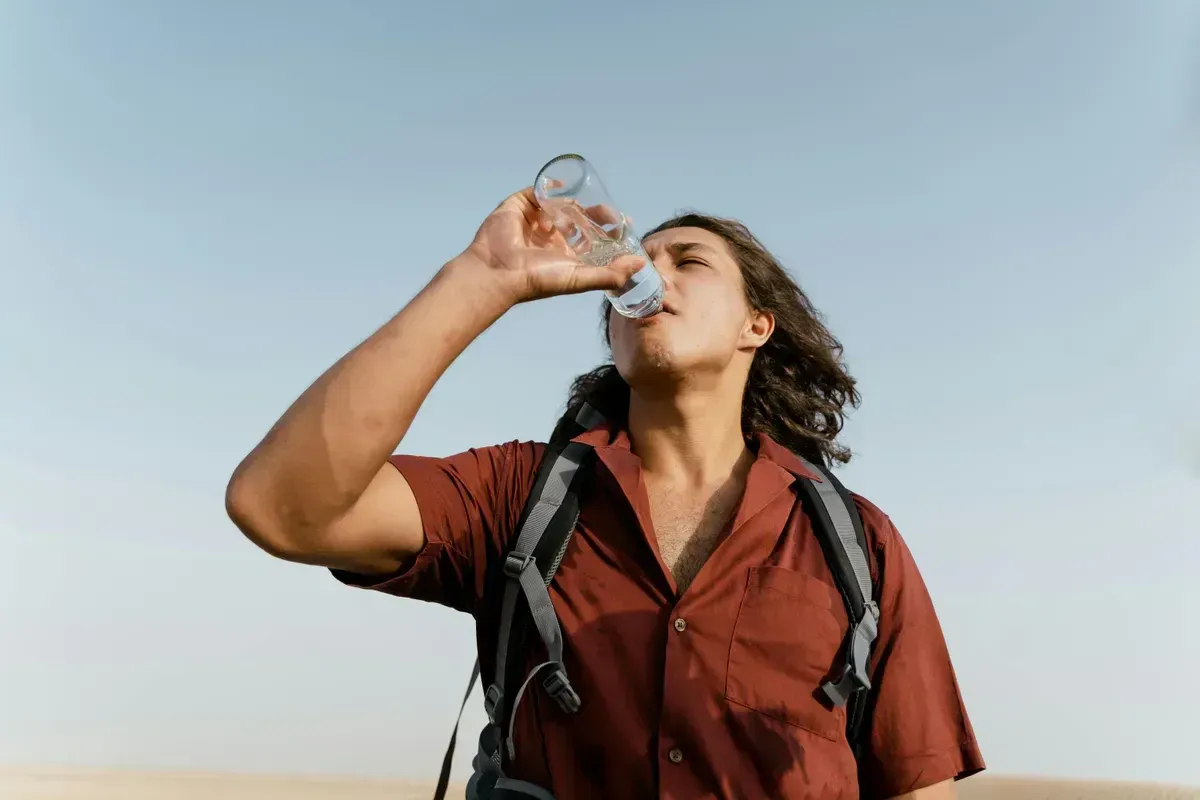 A hiker drinking water from a bottle under a clear sky on a backcountry trail, staying hydrated during an off-grid hike