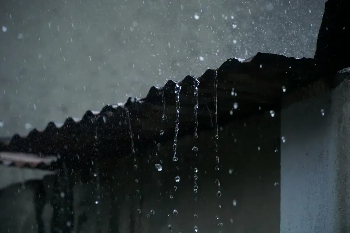 Rainwater cascading off a corrugated metal cabin roof in low evening light, feeding an off-grid rain-collection system